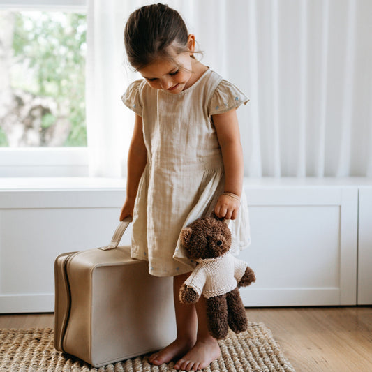 Child holding soft chocolate plush teddy bear in cream wool sweater near window – Mamutino