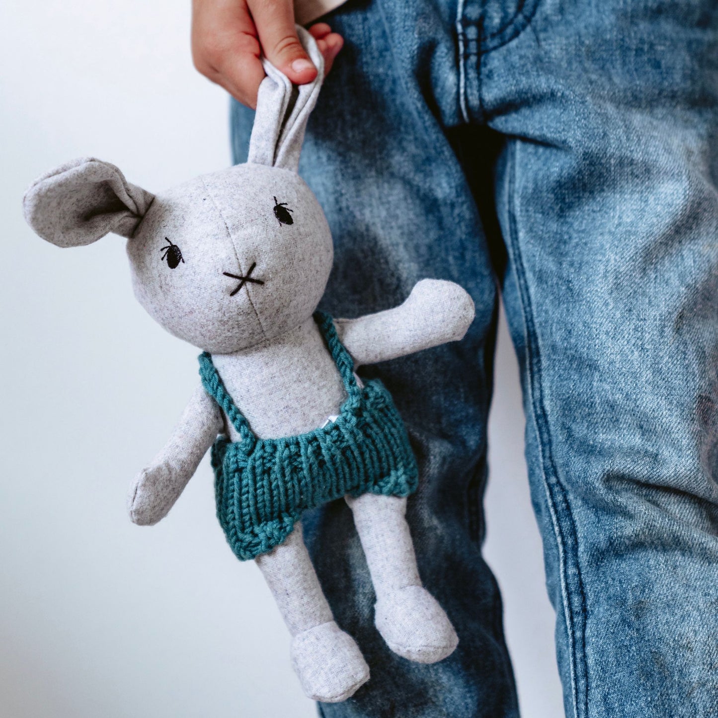 Child holding mini plush bunny toy with knitted blue overalls – Mamutino