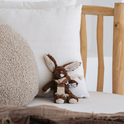 Soft chocolate plush rabbit with wool scarf sitting on nursery bed – Mamutino